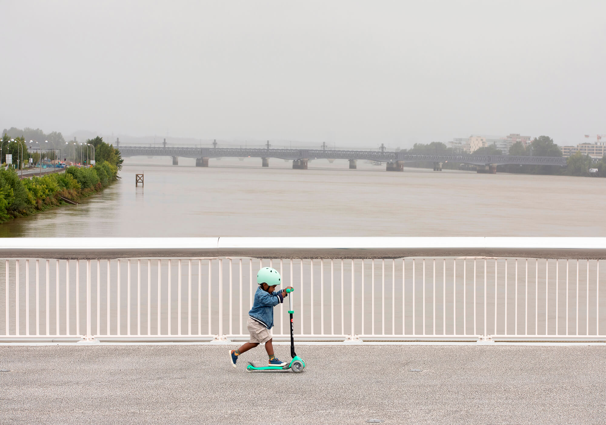 kid scootering across bridge designed by OMA on a foggy day