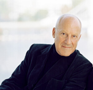 Portrait image of architect Norman Foster wearing a black velvet blazer on a white background.